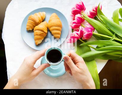 Ragazza con croissant e caffè, un bouquet di tulipani rosa, mattina felice Foto Stock