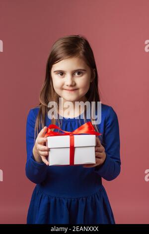 Ragazza carina che tiene un regalo nelle sue mani. Abito blu, sfondo corallo. Buon Natale, San Valentino, buon compleanno e altre festività. Foto Stock