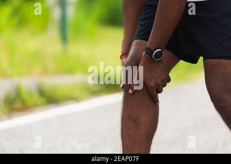 sport runner uomo nero indossare orologio mani giunto tenere ginocchio dolore Foto Stock