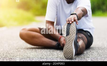 sport runner uomo nero indossare orologio lui seduto tirare la punta piedi che allungano le gambe e il ginocchio Foto Stock