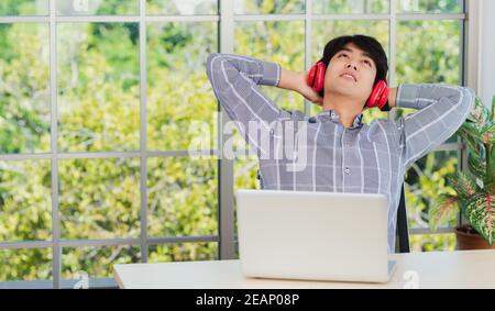 uomo d'affari sorride ascoltando la musica con le cuffie rosse a casa ufficio Foto Stock