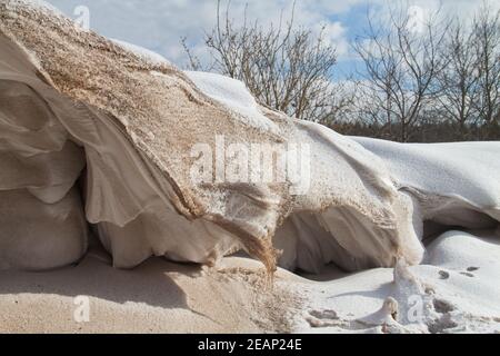 Neve, un deposito di neve e una certa sabbia scolpita dal vento in un tumulo durante una tempesta di neve Foto Stock
