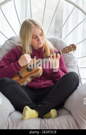 Giovane ragazza adulta che impara a suonare ukulele, apprendimento della chitarra online, messa a fuoco selettiva Foto Stock