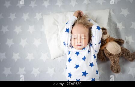 Sei anni bambino che dorme nel letto con la sveglia Foto Stock