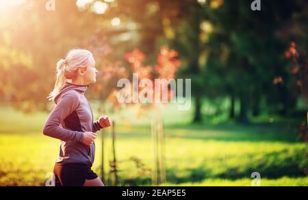 Giovane donna in esecuzione sul campo vicino al mare al tramonto Foto Stock