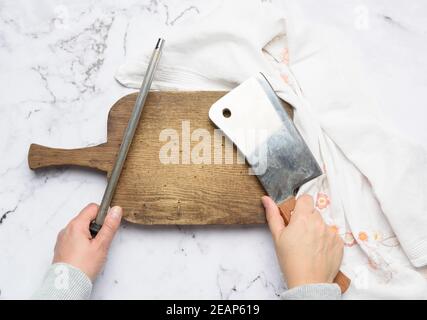 le mani femminili tengono un coltello da cucina e un affilatore con un manico, il processo di affilatura utensili Foto Stock