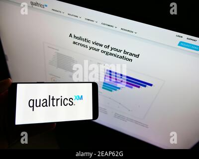 Persona che detiene il cellulare con il logo commerciale della società americana di software Qualtrics International Inc. Di fronte al sito web. Mettere a fuoco il display del telefono. Foto Stock