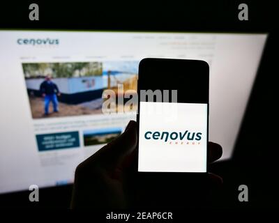 Persona che detiene smartphone con il logo aziendale della società canadese di petrolio e gas Cenovus Energy Inc. Di fronte al sito web. Mettere a fuoco il display del telefono. Foto Stock