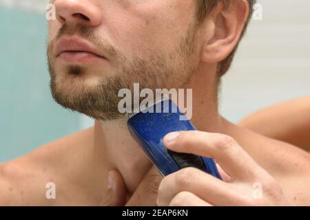 Un uomo taglia una barba sul viso con un regolacapelli, primo piano Foto Stock