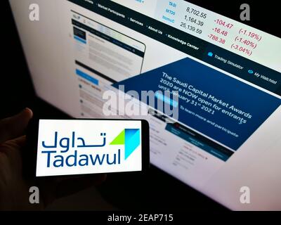 Persona in possesso di smartphone con logo aziendale della borsa Saudita Tadawul sullo schermo di fronte al sito web. Mettere a fuoco il display del telefono. Foto Stock