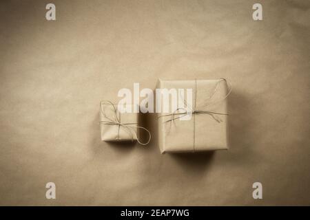 Due scatole regalo avvolte in carta riciclata marrone semplice con corda su sfondo marrone texture vista dall'alto, concetto di presentare e riciclare, spazio di copia, spazio per il testo Foto Stock