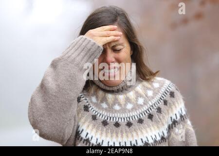 Donna adulta che soffre mal di testa in un parco in inverno Foto Stock