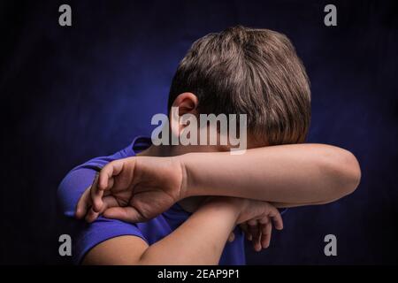 triste adolescente europeo con capelli marrone chiaro negli sport t-shirt viola che ricopre il viso con una mano su isolato sfondo Foto Stock