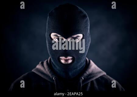 Criminale che indossa balaclava nera e felpa con cappuccio al buio Foto Stock