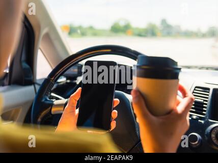 donna che beve caffè caldo takeaway tazza all'interno di una macchina e. tramite smartphone Foto Stock