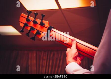 La mano del chitarrista sul collo di una chitarra basso a sei corde. Vista posteriore Foto Stock
