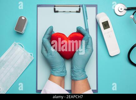 due mani in guanti di lattice blu che tengono un cuore tessile rosso, concetto di donazione Foto Stock