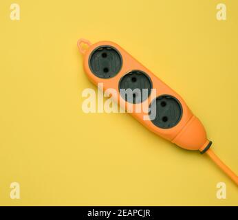 basetta di alimentazione arancione in gomma con tre prese isolate su a. sfondo giallo Foto Stock