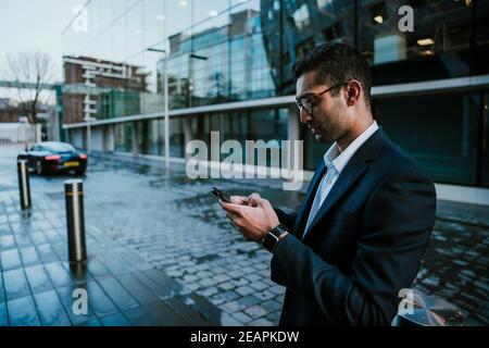 Corsa mista uomo d'affari chattando su smartphone a piedi per lavorare in edificio per uffici Foto Stock
