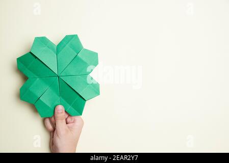 shamrock a quattro foglie di carta, origami, tenuto da una mano di una giovane donna su uno sfondo chiaro. Concetti di fortuna e giorno di San Patrizio. Immagine con c Foto Stock