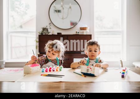 Giovani fratelli seduti a dipingere scatole colorate in moderna sala da pranzo Foto Stock