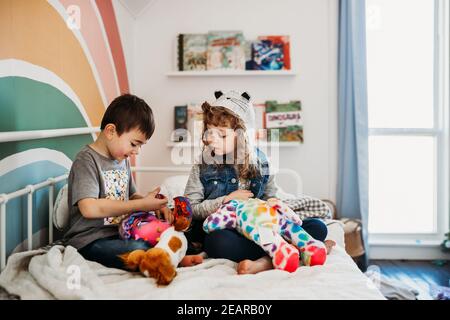 Fratello e sorella seduti sul letto nella camera dei bambini arcobaleno in riproduzione Foto Stock