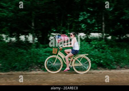 Ragazza che cavalcano la sua bici con una bandiera americana su un Strada sterrata rurale Foto Stock