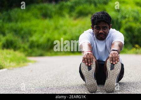 sport runner uomo nero indossare orologio lui seduto tirare la punta piedi che allungano le gambe e il ginocchio Foto Stock