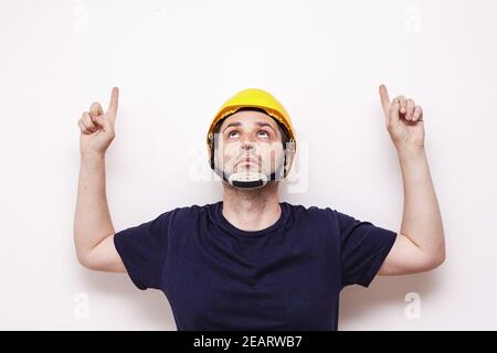 Lavoratore caucasico che indossa un casco giallo e le dita rivolte verso l'alto isolato su sfondo bianco Foto Stock