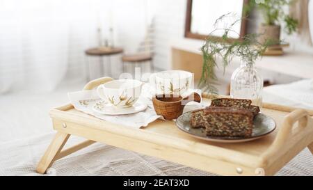 Colazione preparata da vicino in camera. Tazze su un vassoio con vaso sul letto. Messa a fuoco selettiva. Stile scandinavo. Foto Stock