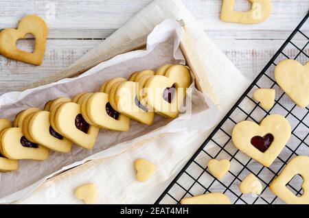 Biscotti a forma di cuore con confettura di lamponi e vaniglia in una scatola di legno e su una rastrelliera nera con un tovagliolo bianco. Foto Stock