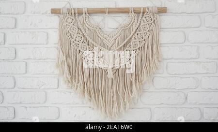 Pannello parete nello stile di Boho fatto di fili di cotone in colore naturale su una parete di mattoni bianchi. Bellissimo pannello a muro boho macrame per un'atmosfera accogliente Foto Stock