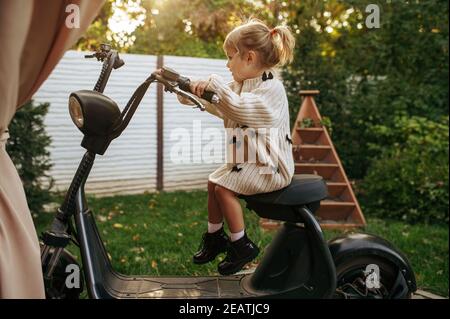 Bambina seduta su scooter d'epoca in giardino Foto Stock