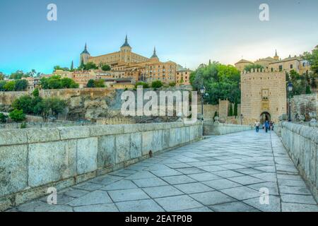 Vista al tramonto del ponte di Alcantara sul fiume Tajo con il castello di Alcazar sullo sfondo a Toledo, Spagna Foto Stock