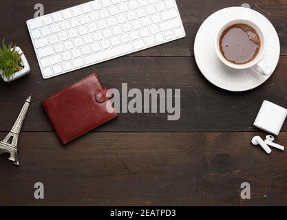 tastiera wireless bianca, cuffie wireless e portafoglio in pelle marrone su un tavolo di legno marrone Foto Stock