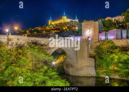 Vista notturna del ponte di Alcantara sul fiume Tajo con il castello di Alcazar sullo sfondo a Toledo, Spagna Foto Stock