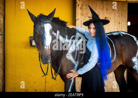 Una ragazza vestita come una strega si trova accanto a un cavallo su cui uno scheletro è dipinto in vernice bianca Foto Stock