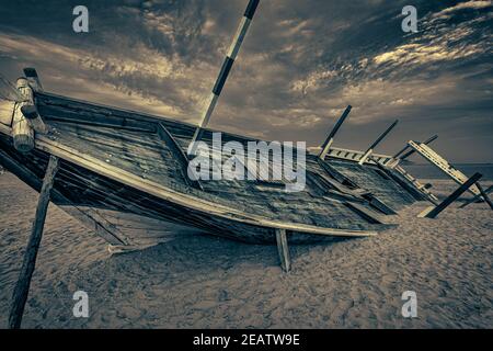 Vecchia barca araba in legno (dhow) intrecciata sulla spiaggia nera e bianco immagine ravvicinata con nuvole nel cielo Foto Stock