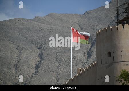 Il Forte Nakhal Nakhl è una grande fortezza ai piedi dei Monti Hadshar nella regione di al Batinah, Oman. Una bandiera Omani vola di fronte alle fortificazioni. Foto Stock