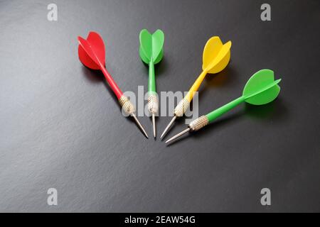 dartboard e freccette rosse, verdi e gialle su sfondo nero Foto Stock