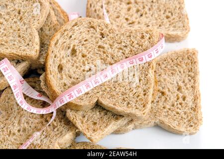 Contro un eccessivo aumento di peso a casa, pane crusca, fette di pane crusca e un metro a nastro Foto Stock