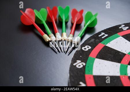 dartboard e freccette rosse, verdi e gialle su sfondo nero Foto Stock