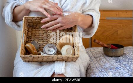 La donna gode il rituale domestico piccolo della stazione termale, le mani creaming con il prodotto organico di formula di erbe dopo il bagno. Cura meditativa di sé. Concetto di azienda agricola a faccia. Foto Stock