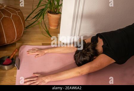 Dopo una lezione di yoga su smartphone, donna in posa più rilassante del bambino che pratica sul tappeto yoga a casa. Primo piano. Foto Stock