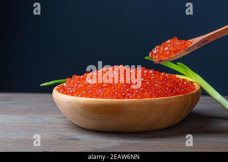 Caviale rosso in una tazza di legno su fondo di legno con un cucchiaio. Foto Stock