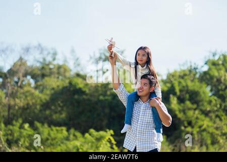 padre e portando una ragazza eccitata sulle spalle che si divertono e godendo lo stile di vita all'aperto insieme giocando giocattolo aereo Foto Stock