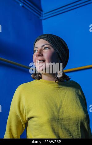 felice sorridente giovane ragazza bruna adolescente in maglia cap e. maglia gialla su sfondo blu Foto Stock