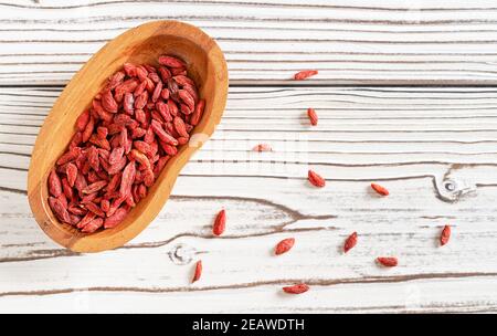 Goji secco aka. Semi di mirtillo in ciotola di legno e versato su tavole bianche scrivania vicino Foto Stock