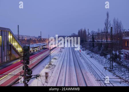 Paesaggio notturno all'aperto e vista dall'alto sulla stazione ferroviaria a piattaforma, sulla pista ferroviaria coperta di neve e sul movimento del treno regionale nella stagione invernale. Foto Stock