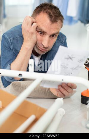 scioccato giovane uomo confuso circa l'assemblaggio dei mobili Foto Stock